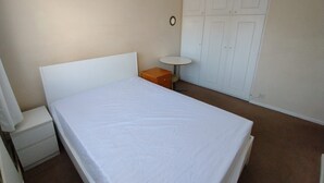 A bedroom with a bed, a nightstand, a small round table, and a wardrobe. - Lovely Double Bedroom - Putney (London)