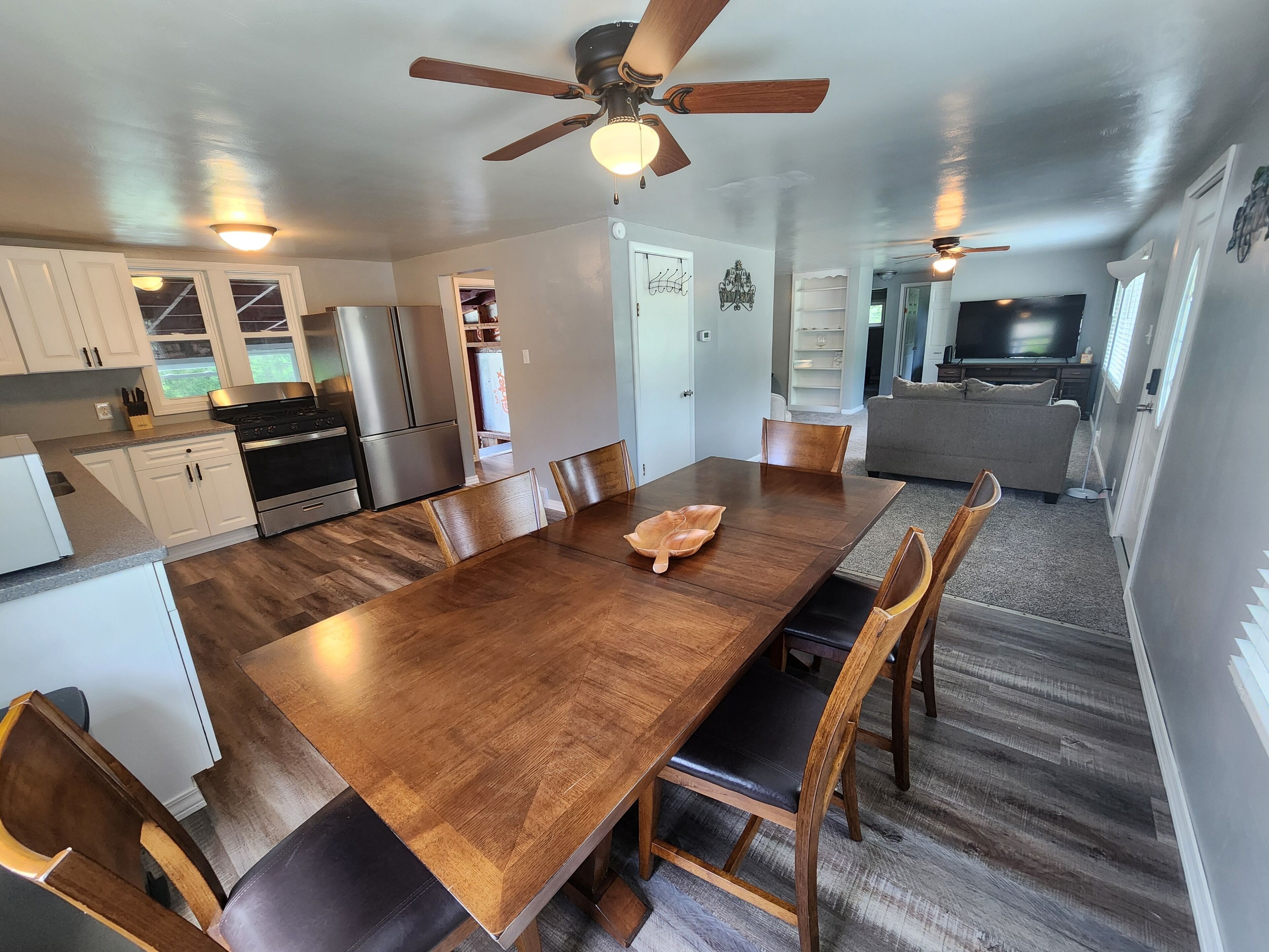 Une cuisine spacieuse avec des meubles blancs, une grande table à manger en bois et un ventilateur de plafond.