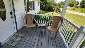 Eine Veranda mit zwei Korbstühlen und einem kleinen Tisch, einer weißen Tür und einer Fußmatte.