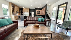 A modern living room with a brown leather sofa, a wooden coffee table, and a large window. - The Reserve at Kirby Landing (Kirby)