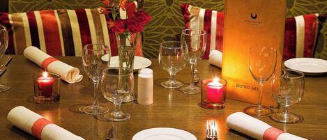 A dining table set with wine glasses, plates, and candles, with a menu stand and a vase of flowers.