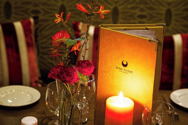 A candlelit table with a menu, a vase with red roses, and a salt and pepper shaker.