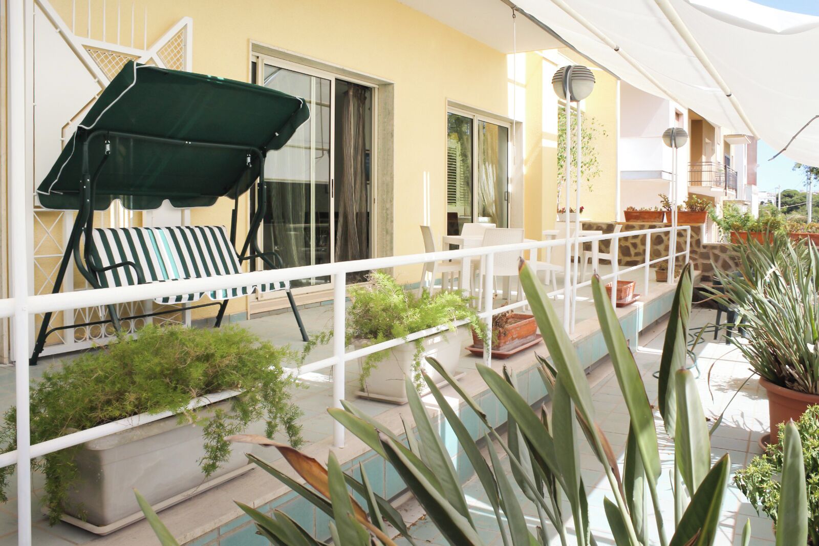 A balcony with a green umbrella, a striped chair, and potted plants.