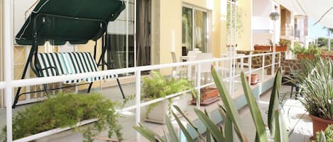 A balcony with a green umbrella, a striped chair, and potted plants.