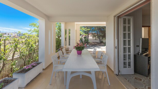 Un coin repas avec une table et des chaises blanches, une plante en pot et une vue sur l’extérieur.