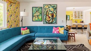 A living room with a blue sofa, a glass coffee table, and two abstract paintings on the wall.