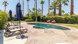A swimming pool with lounge chairs and umbrellas, surrounded by palm trees and a well-maintained garden.