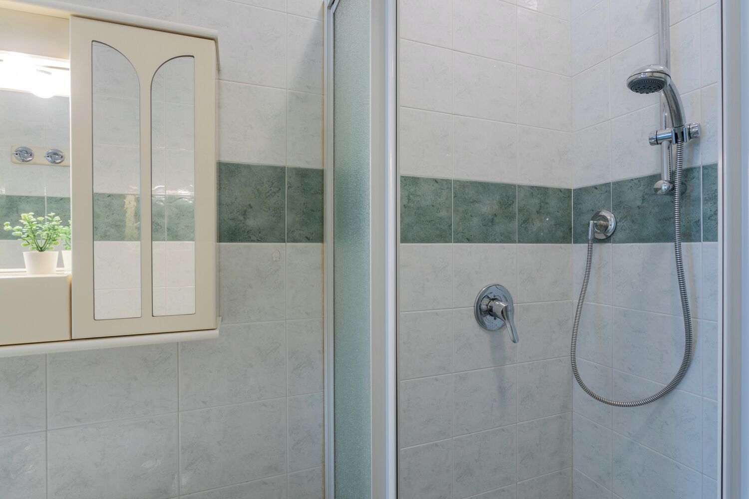 A bathroom with a glass shower enclosure, a toilet, and a sink with a mirror.