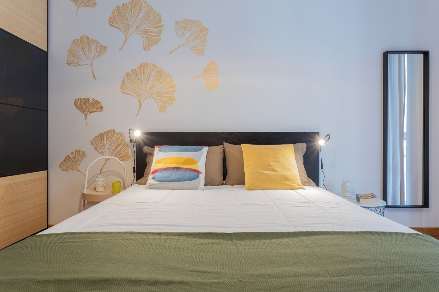 Una camera da letto moderna con un letto, una testiera, un comodino, una lampada e uno specchio.