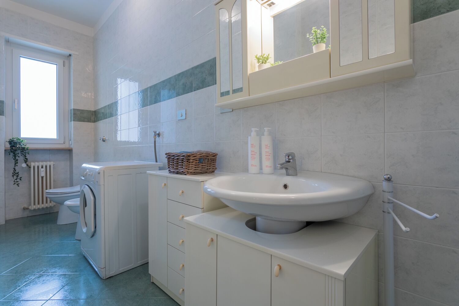 A modern bathroom with a washing machine, a sink, and a mirror.