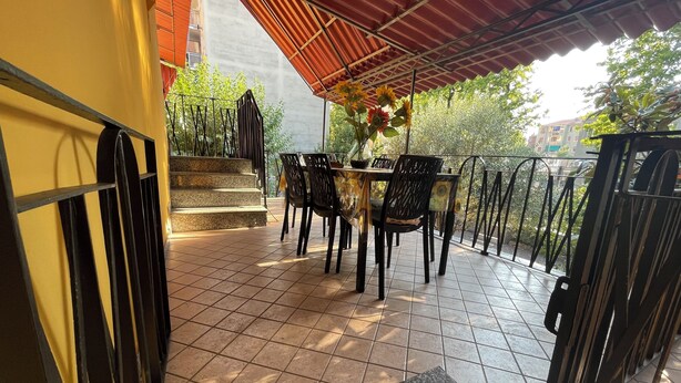 A covered outdoor seating area with a table and chairs, a potted plant, and a staircase leading to an upper level. - 75sqm apartment in villa (Cinisello Balsamo)