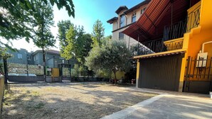 A residential area with a paved driveway, a gated entrance, and a yellow building with a red roof. - 75sqm apartment in villa (Cinisello Balsamo)