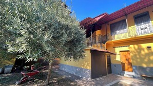 A yellow building with a red roof, a balcony with metal railings, and a tree in the foreground. - 75sqm apartment in villa (Cinisello Balsamo)