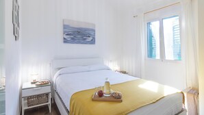 A neatly made bed with a yellow blanket, a bedside table with a lamp, and a tray with a drink and fruit.