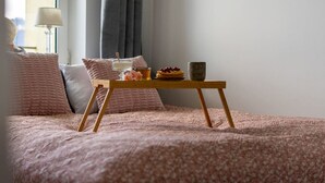 A neatly made bed with a pink floral bedspread, a wooden bedside table with a bowl of fruit and a cup, and a lamp in the background. - Warsaw Central Apt - 9th Floor, Balcony, Tram&Bus - by Rentujemy (Warszawa)