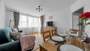A modern living room with a teal sofa, a wooden dining table set with plates and glasses, and a TV on a wooden cabinet. - Warsaw Central Apt - 9th Floor, Balcony, Tram&Bus - by Rentujemy (Warszawa)