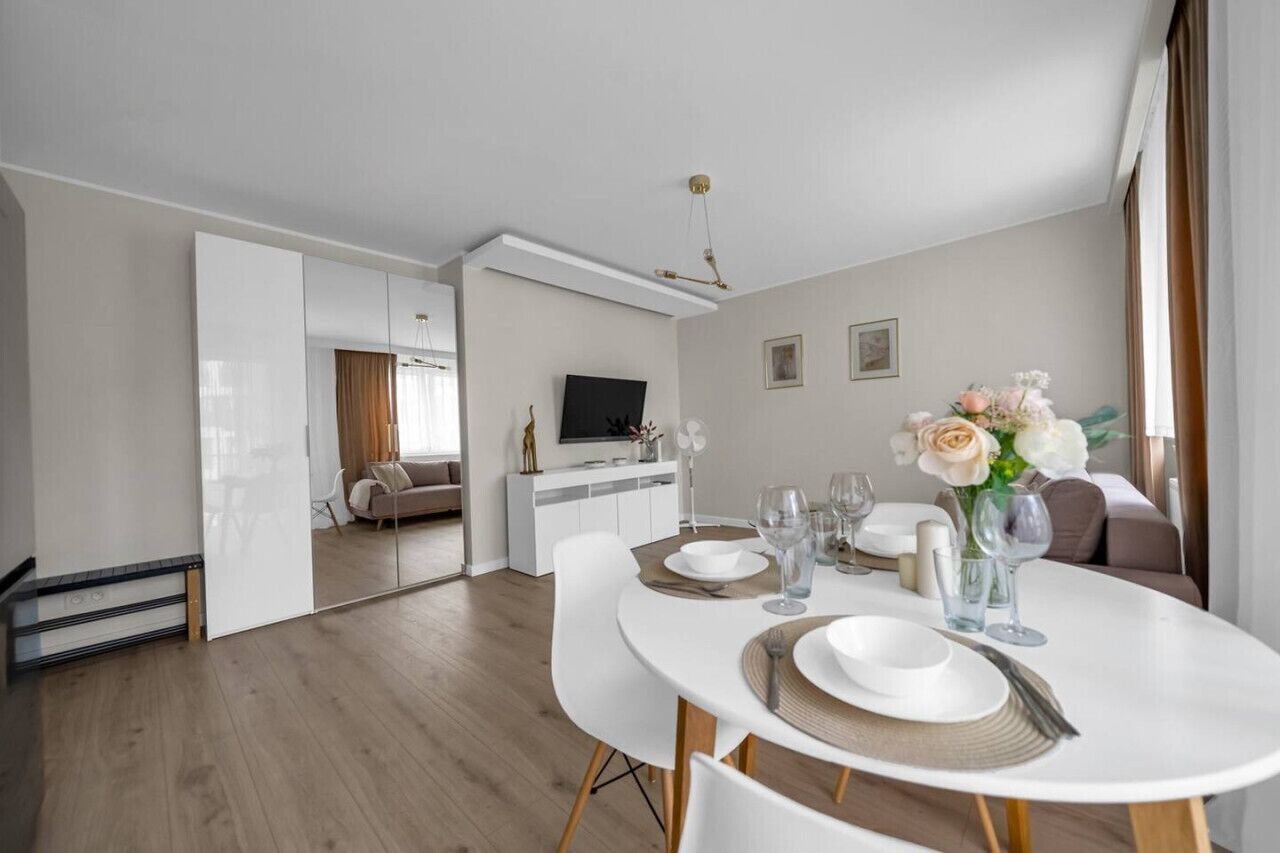 Una sala de estar moderna con comedor, un juego de sofá, un televisor de pantalla plana y un florero decorativo con flores.