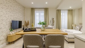 Un salon moderne avec une table à manger en bois, deux fauteuils, un canapé et un téléviseur fixé au mur.