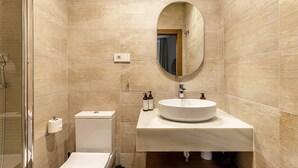 Une salle de bain moderne avec des carreaux de couleur beige, un miroir rond, un lavabo et des toilettes.