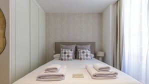 A neatly made bed with two pillows, a bedside lamp, and two folded towels on the bed.