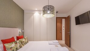 Un dormitorio con cama, almohadas, lámpara colgante, armario y televisor en la pared.