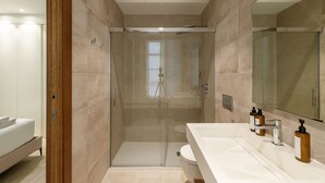 Un baño moderno con cabina de ducha de vidrio, un lavabo blanco con artículos de aseo y un espejo grande.