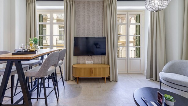 Una sala de estar moderna con comedor, un televisor de pantalla plana en la pared y un ventanal con cortinas.