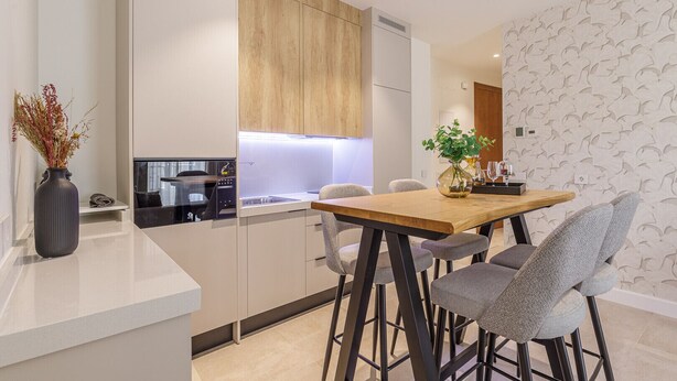 Una cocina moderna con horno empotrado y comedor con mesa de madera y sillas grises.