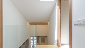Un intérieur moderne avec un escalier en verre, une porte en bois et une vue sur l’extérieur.