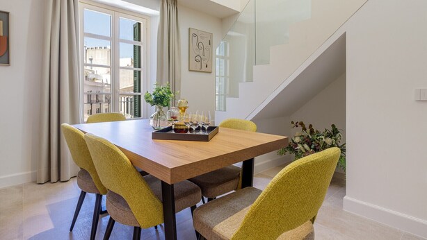 Un coin repas avec une table en bois et des chaises jaunes, un vase rempli de fleurs et un plateau avec des verres et une bouteille.