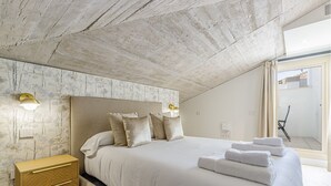 Une chambre avec un grand lit, une table de chevet, une tête de lit dotée de lampes fixées au mur et une vue sur l’extérieur.