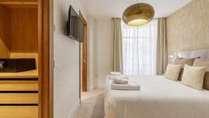 Hotelkamer met een bed, een aan de muur bevestigde televisie, een houten garderobe en een groot raam met gordijnen.