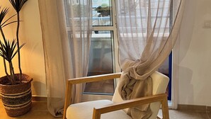 Ein Zimmer mit einem Schaukelstuhl aus Holz, einer Topfpflanze und durchsichtigen Vorhängen.