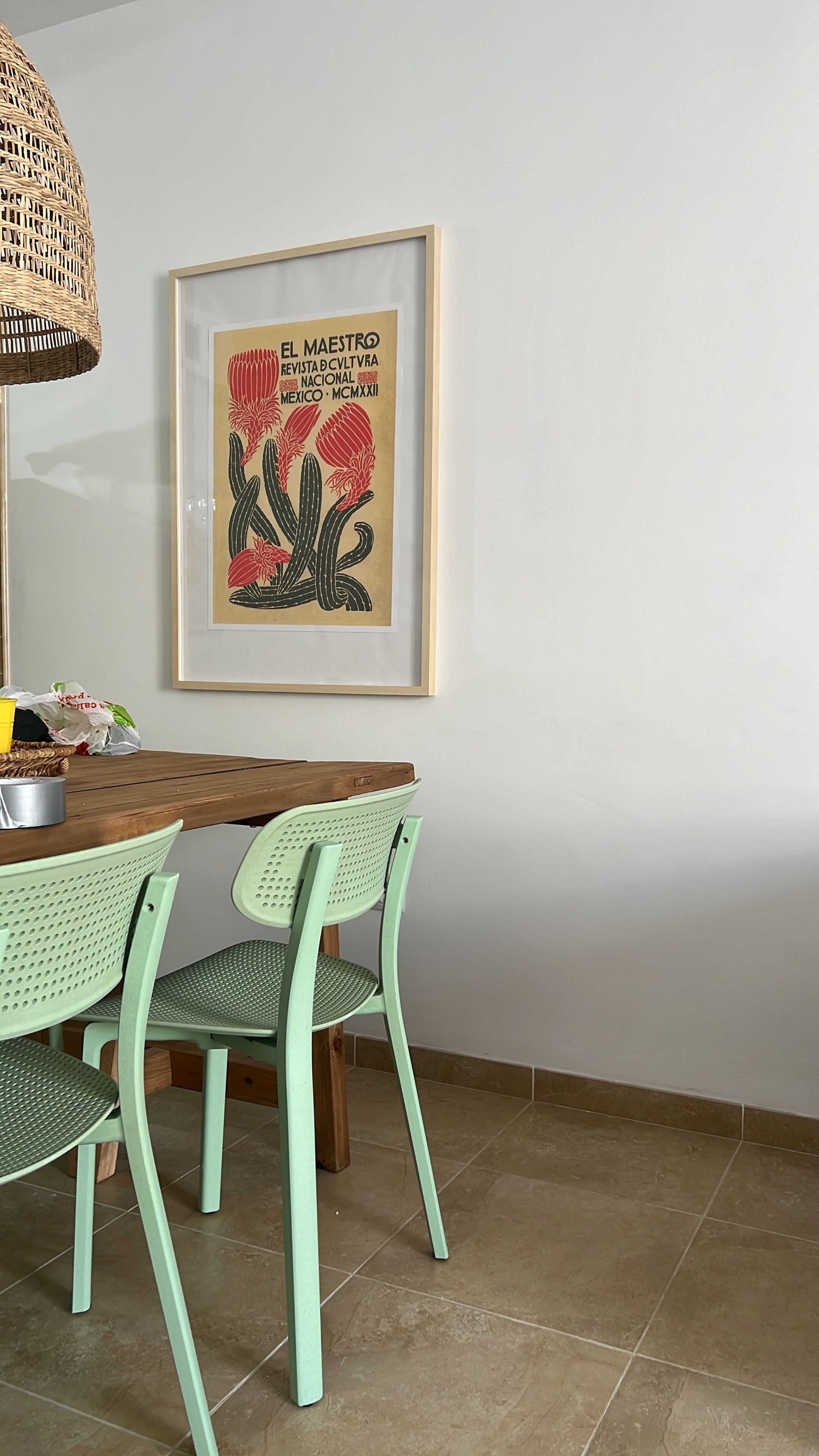 A dining area with a wooden table, green chairs, and a framed poster on the wall.
