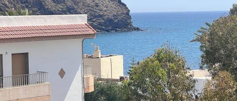 A coastal building with a red-tiled roof, a balcony, and a view of the sea.
