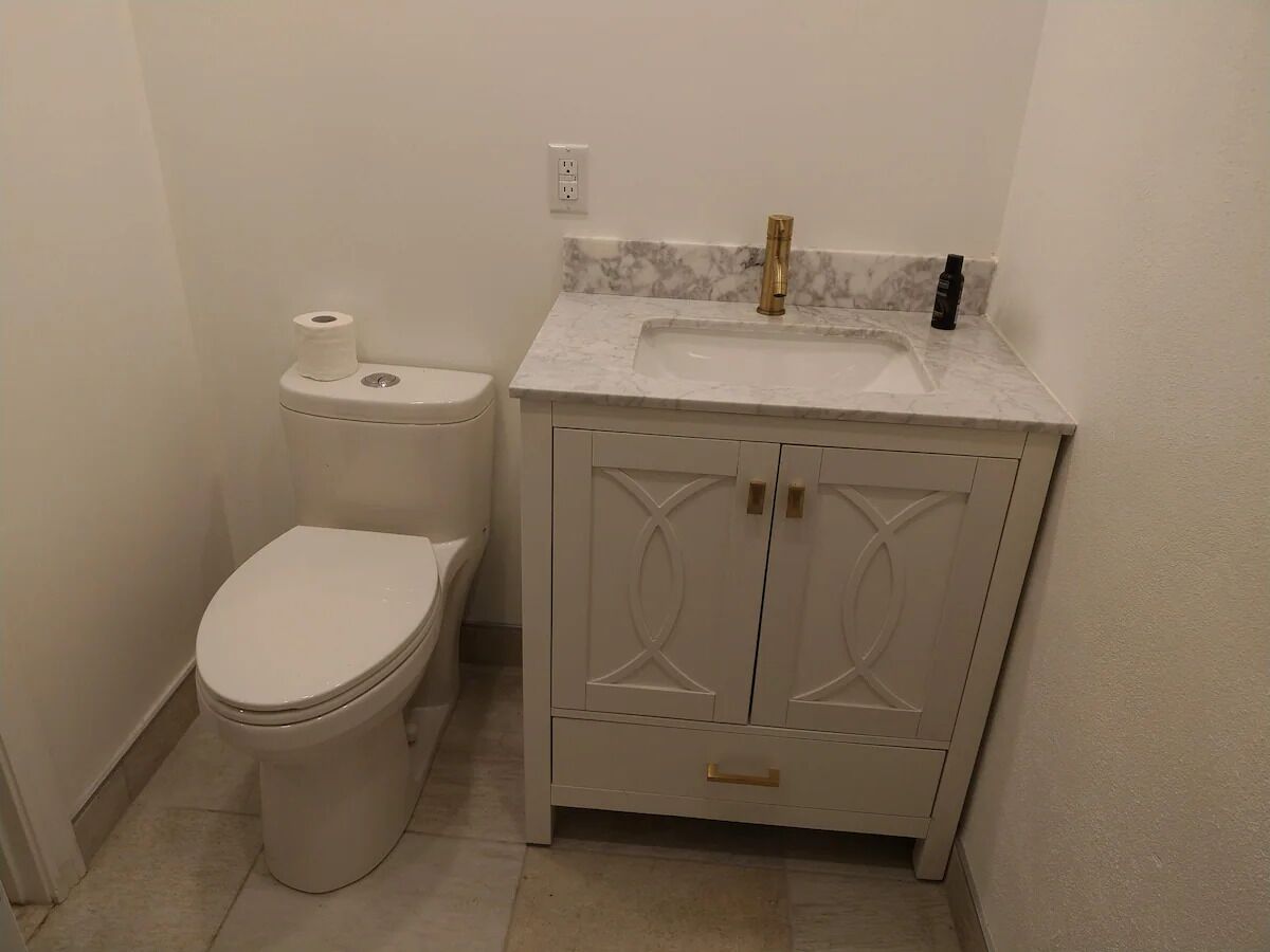A bathroom with a toilet, a sink with a marble countertop, and a cabinet with decorative doors.