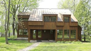 A modern wooden house with a sloped roof, large windows, and a paved entrance.