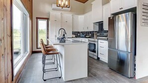 Een moderne keuken met witte kasten, een roestvrijstalen koelkast en een groot keukenblok met barkrukken.