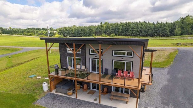 Een modern herenhuis met twee verdiepingen, een balkon, buitenmeubilair en uitzicht op een groen veld.