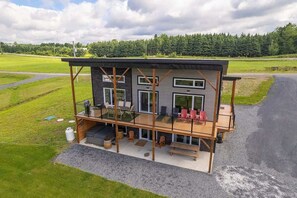 Uma casa moderna de dois andares com varanda, área de estar ao ar livre e vista para um campo verde.
