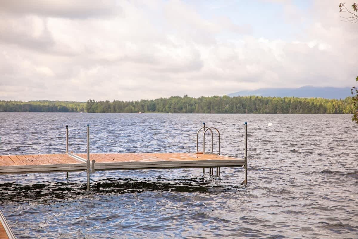 Un moll de fusta que s'endinsa en un llac, amb una barana i un pal de metall.