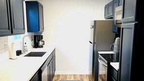 A compact kitchen with dark cabinets, a stainless steel refrigerator, a built-in oven, and a coffee maker. - Family home in Dallas’s most prestigious neighborhood - Preston Hollow! 3 BR/2BA (Dallas)