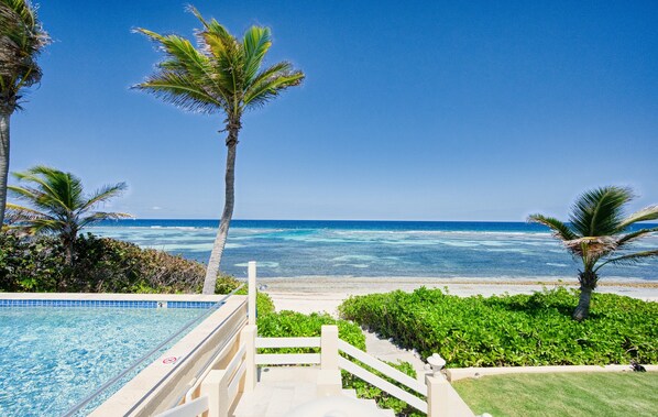 A pool area with a view of the ocean and palm trees. - Coral Loft 4BR + 1 BR Oceanfront Villa w/ Private Pool & Beach in Grand Cayman (Rum Point)