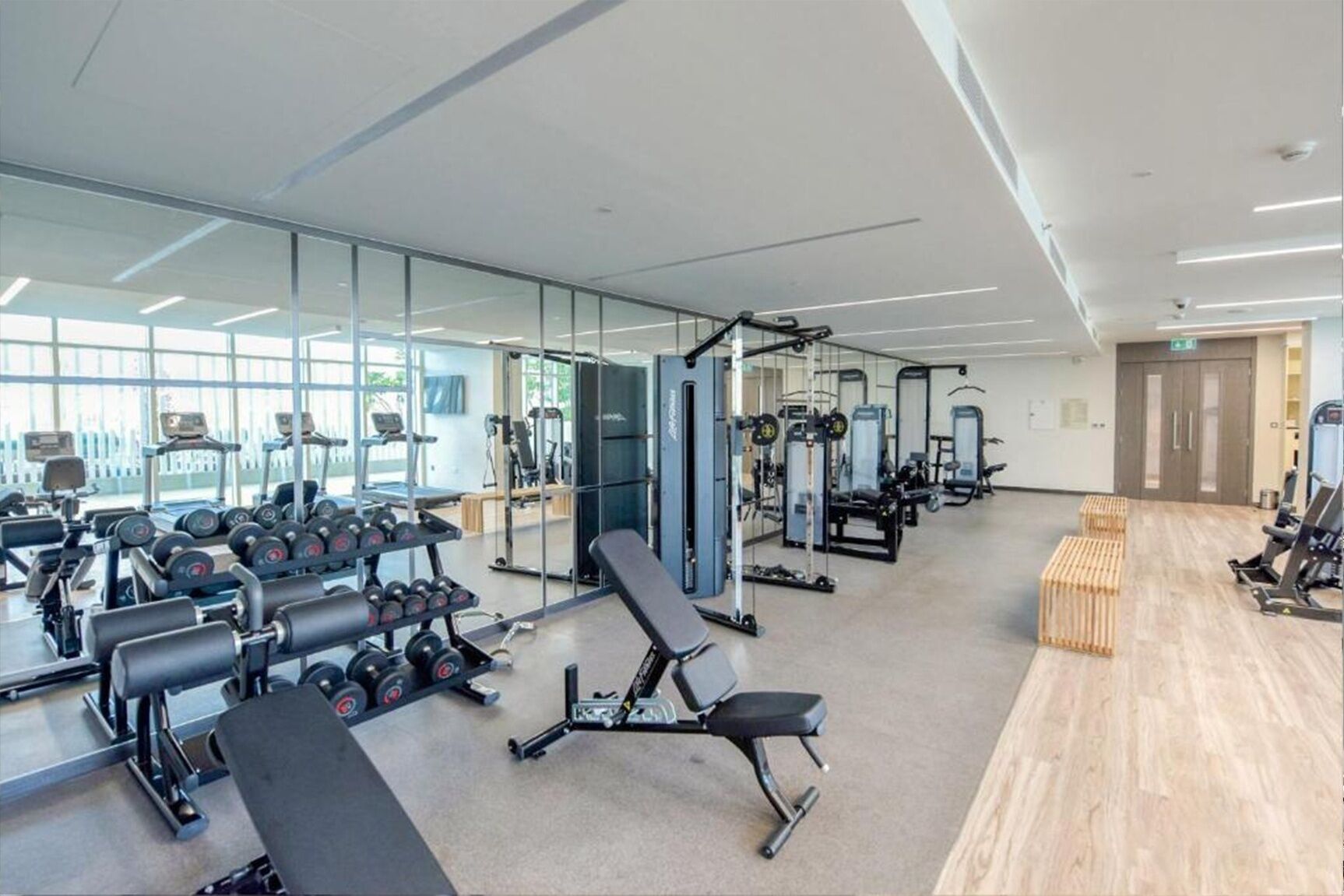 Ein modernes Fitnessstudio mit verschiedenen Trainingsgeräten, Spiegelwänden und Holzboden.