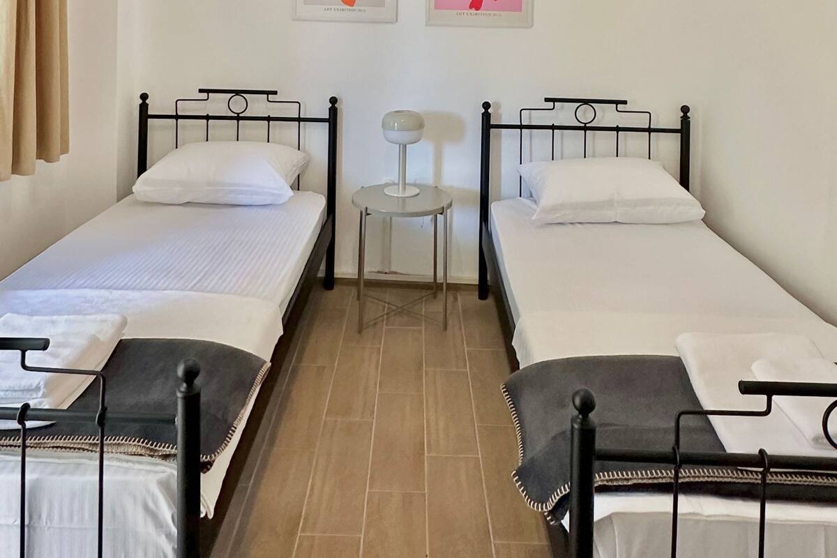 A room with two single beds, a small table, and two wall-mounted artworks.