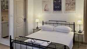A hotel room with a bed, two bedside tables with lamps, a door, and three framed pictures on the wall. - Denizhan Bağ Evi (Bozcaada)