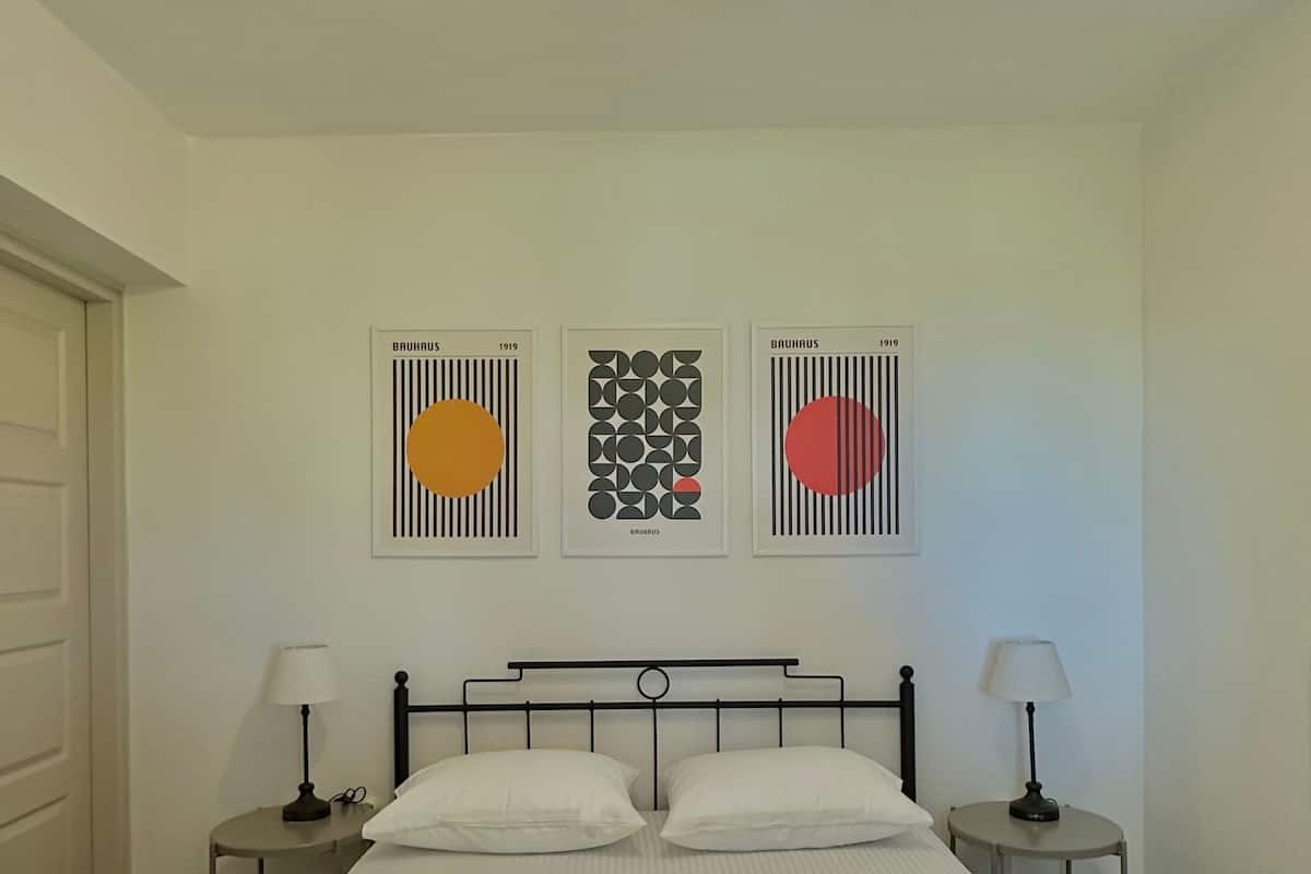 A bedroom with a large bed, two bedside tables with lamps, and three framed artworks on the wall.