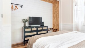 Un dormitorio con cama, cómoda, televisor y techo de madera.