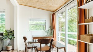 Un comedor con una mesa y sillas, una planta en maceta y vistas a través de un ventanal grande.