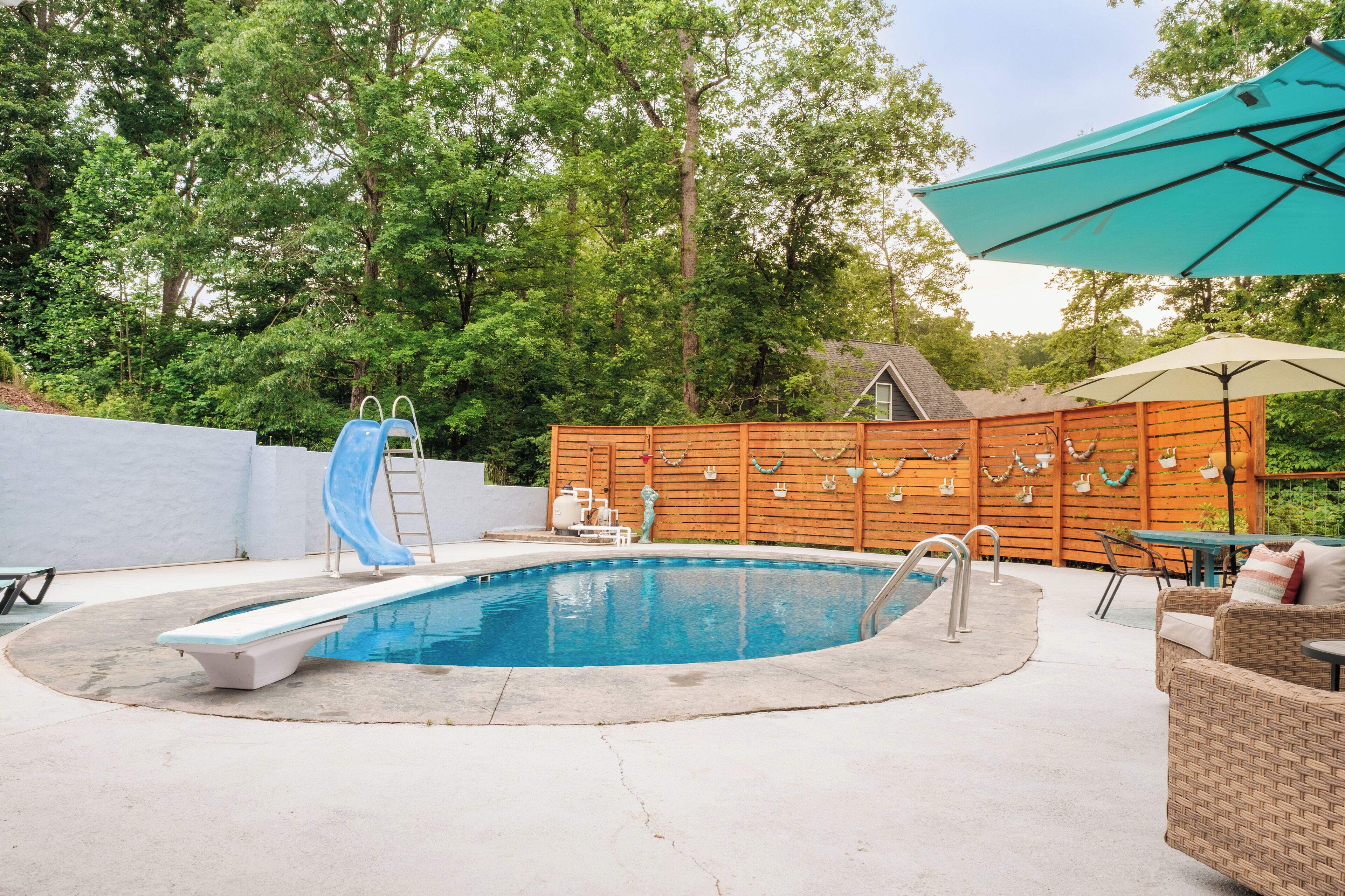 Una piscina con tobogán, rodeada por una valla de madera, y una mesa con sillas.